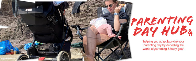 Mum sitting on a chair at the beach feeding baby with a 3 wheeled stroller in the foreground - parenting day hub -  philandteds.com